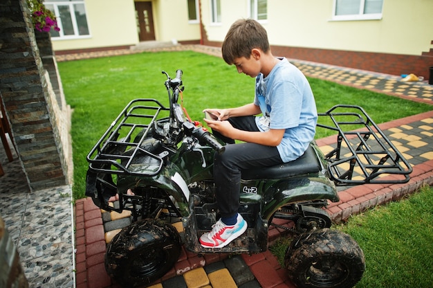 Garçon en quad ATV à quatre roues avec téléphone mobile.