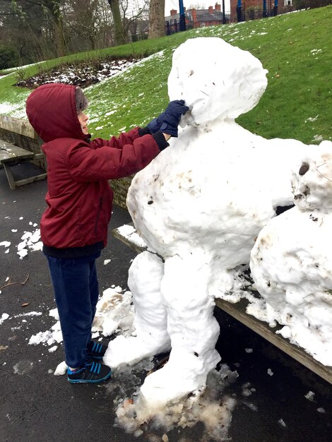 Photo le garçon qui fait un bonhomme de neige dans le parc