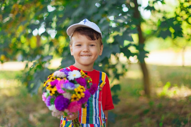 Garçon qui rit avec un bouquet de fleurs un enfant avec un bouquet de fleurs sauvages pour maman un cadeau a surpr...