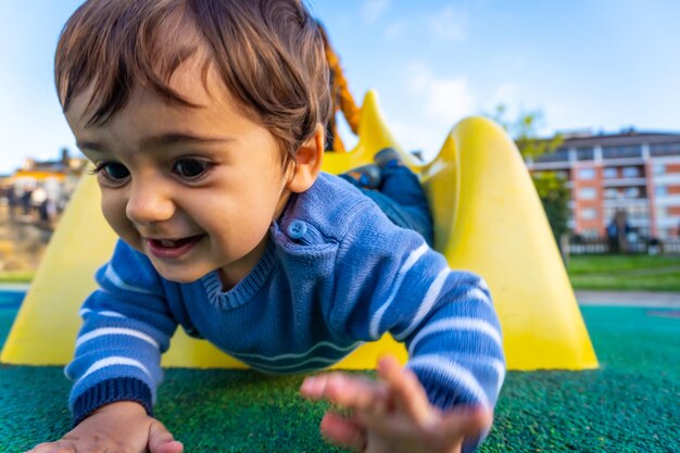 Un garçon de race blanche d'un an souriant et jouant des balançoires jouant dans le parc en sautant sur un couineur jaune