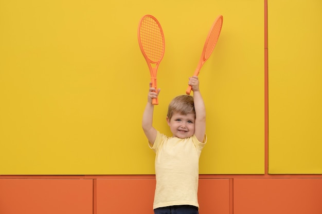 Garçon avec des raquettes de tennis contre le mur jaune