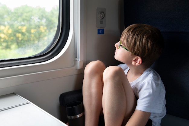 Garçon réfléchi est assis dans le chariot de compartiment et regarde dans la fenêtre