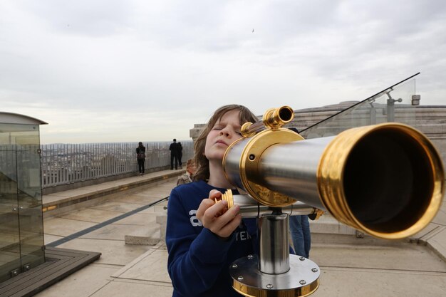 Photo un garçon regardant à travers un binocule à pièces contre le ciel