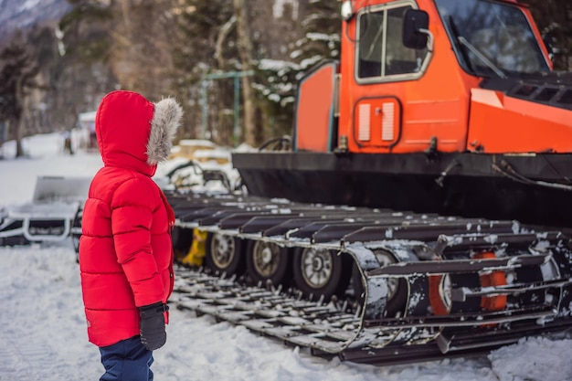 Un garçon regarde un snowcat dans une station de ski