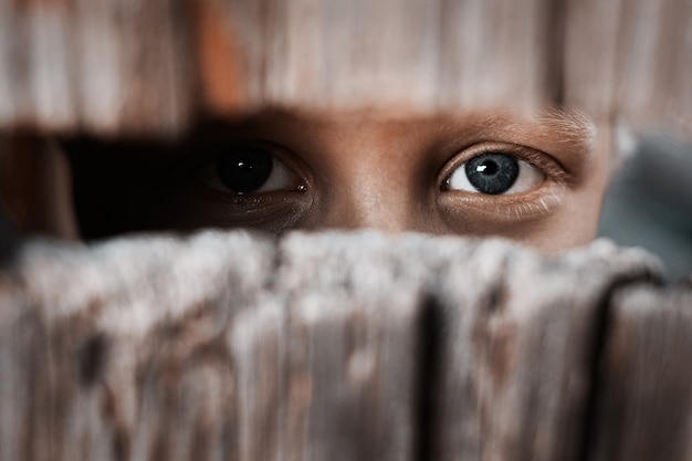 Un garçon regarde à travers le trou dans la clôture