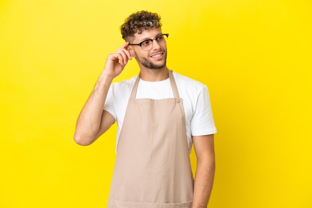 Garçon de restaurant homme blond isolé sur fond jaune pensant à une idée