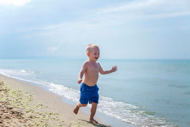 Un garçon riant en short bleu court le long du rivage de sable sur une journée ensoleillée Bonheur positif vacances à la station et un style de vie actif