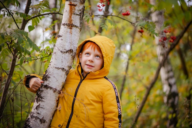 Garçon roux de huit ans dans une veste jaune dans la forêt d'automne