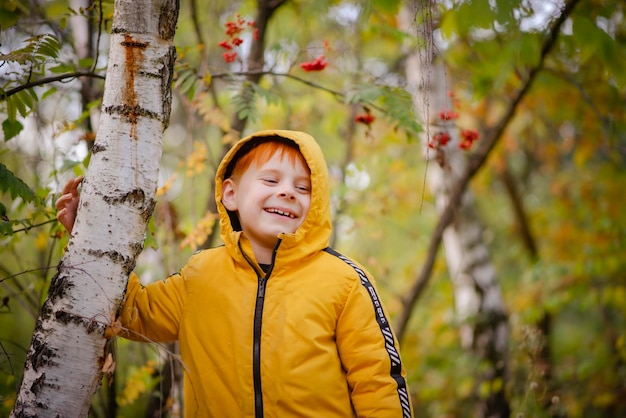 Garçon roux de huit ans dans une veste jaune dans la forêt d'automne