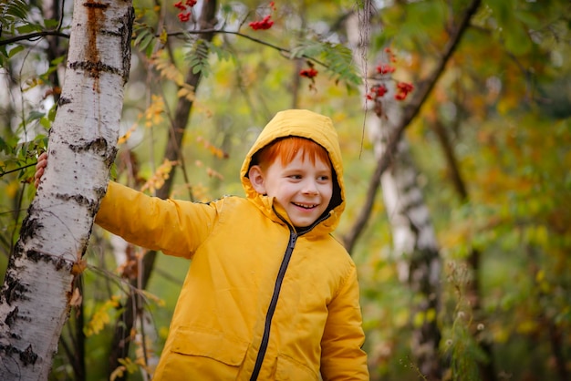 Garçon roux de huit ans dans une veste jaune dans la forêt d'automne