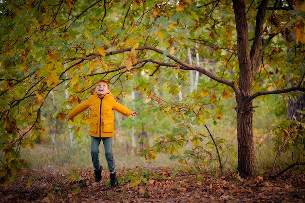 Garçon roux de huit ans dans une veste jaune dans la forêt d'automne