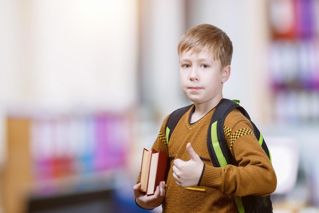 Un garçon avec un sac à dos et un livre qui lève le pouce.