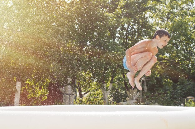 Garçon sautant dans la piscine du jardin en été