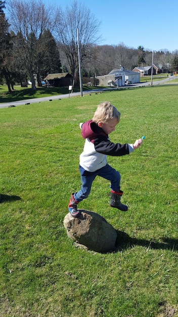 Un garçon sautant d'un rocher sur un champ herbeux dans un parc.