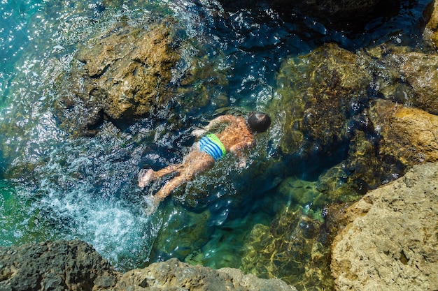 Un garçon saute de la falaise dans la mer par une chaude journée d'été Vacances sur la plage Le concept de tourisme actif et de loisirs