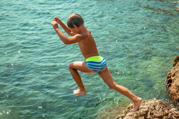 Un garçon saute de la falaise dans la mer par une chaude journée d'été. Vacances à la plage. Le concept de tourisme actif et de loisirs