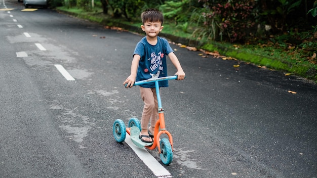 Un garçon sur un scooter de poussée sur la route de la ville