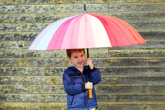 Photo un garçon se cachant sous un parapluie multicolore par temps de pluie, gros plan d'un enfant réjouissant qui se cachait de la pluie