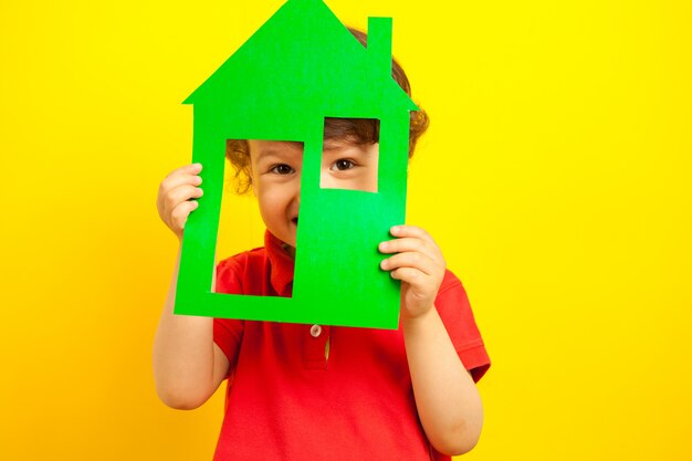 Le garçon se cache dans une maison en carton. enfant dans une veste rouge vif.