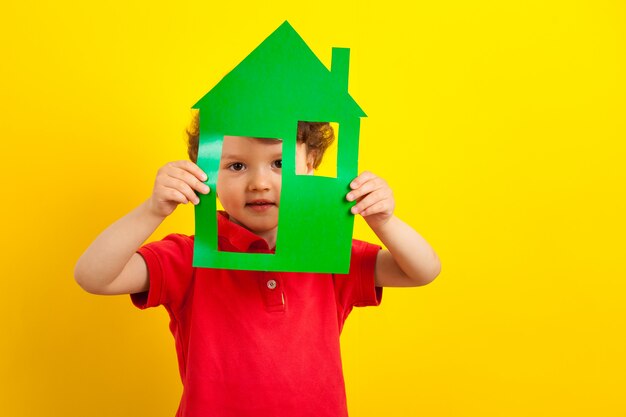 Le garçon se cache dans une maison en carton. enfant dans une veste rouge vif.