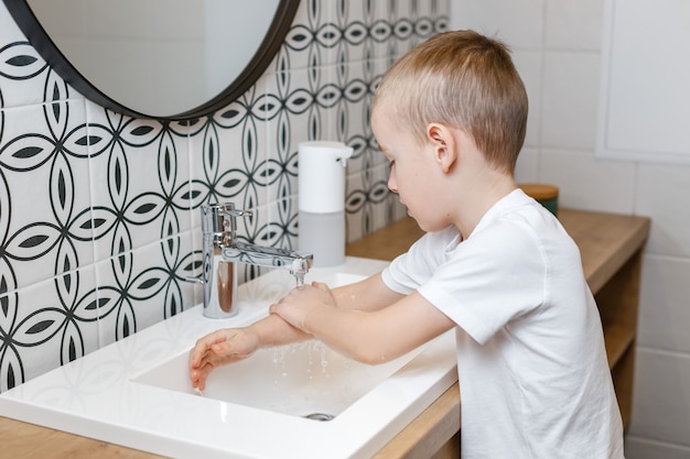 Photo garçon se laver les mains dans la salle de bain à l'aide d'un distributeur de savon à capteur.