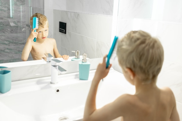 Le garçon se peigne les cheveux devant le miroir le matin dans le bain, hygiène le matin
