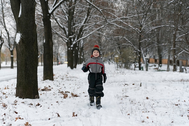 Garçon se promène dans le parc d'hiver couvert de neige. Marcher avec des enfants en hiver.