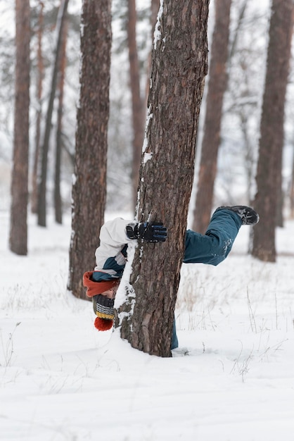 Garçon se promène dans le parc et se cache derrière l'arbre Enfant s'amuse dans le parc d'hiver Cadre vertical