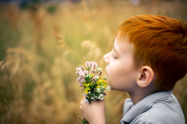 Un garçon de sept ans aux cheveux roux avec un bouquet de fleurs sauvages en été