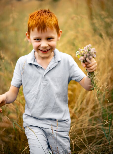 Un garçon de sept ans aux cheveux roux avec un bouquet de fleurs sauvages en été