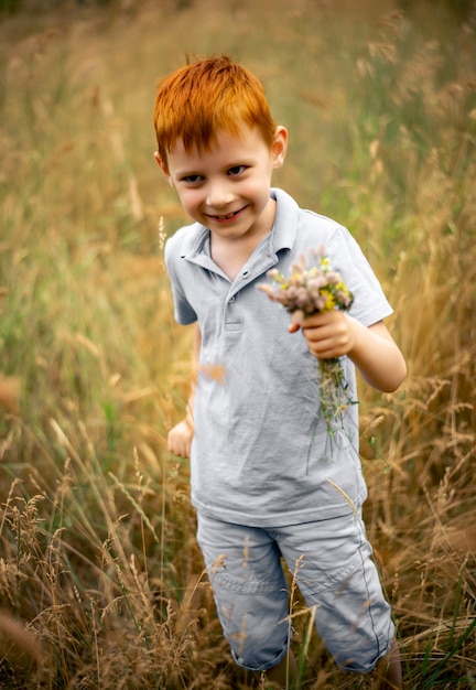 Photo un garçon de sept ans aux cheveux roux avec un bouquet de fleurs sauvages en été