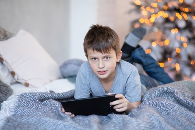 Un garçon sérieux tient une tablette dans ses mains. enfant joue à des jeux informatiques sur la tablette