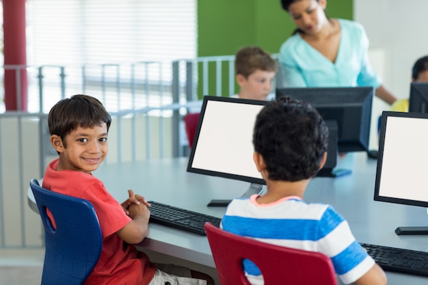 Garçon avec ses camarades de classe et enseignant pendant les cours d'informatique