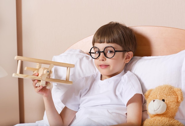 Garçon de six ans avec un avion en bois dans son lit