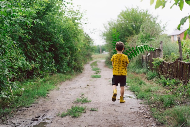 Un garçon de six ans court avec des feuilles vertes dans ses mains dans la campagne Joyeux enfant garçon riant et jouant pendant la journée d'été Vue arrière