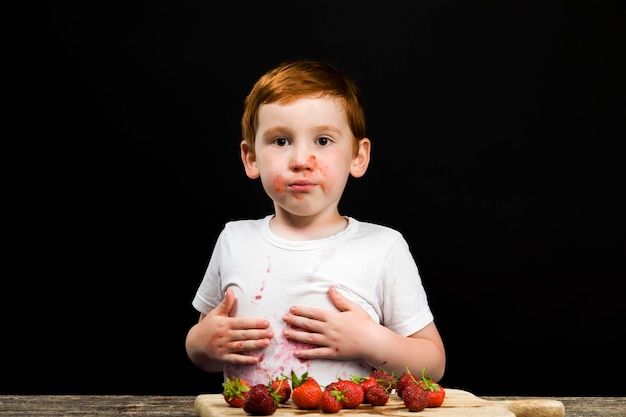 Un garçon de six ans avec des fraises rouges mûres