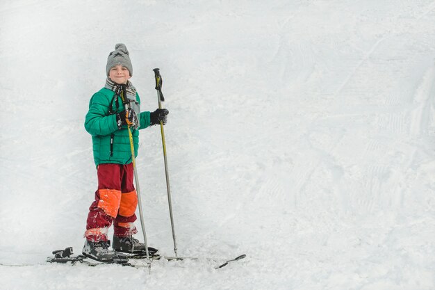 Le garçon sur des skis avec des bâtons de ski sourit.