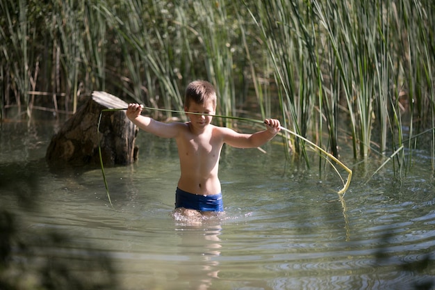 Garçon solitaire admirant la beauté du lac d'été en grèce Garçon jouant à l'extérieur imitant la pêche dans un lac