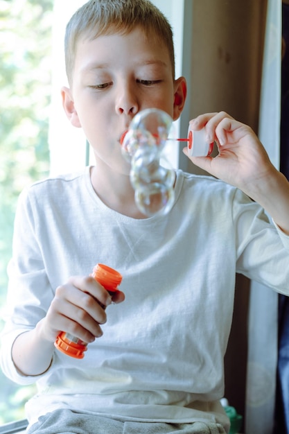 Garçon soufflant des bulles de savon assis sur un canapé à la maison beaucoup de bulles de savon Jeux intéressants à la maison bulles magiques