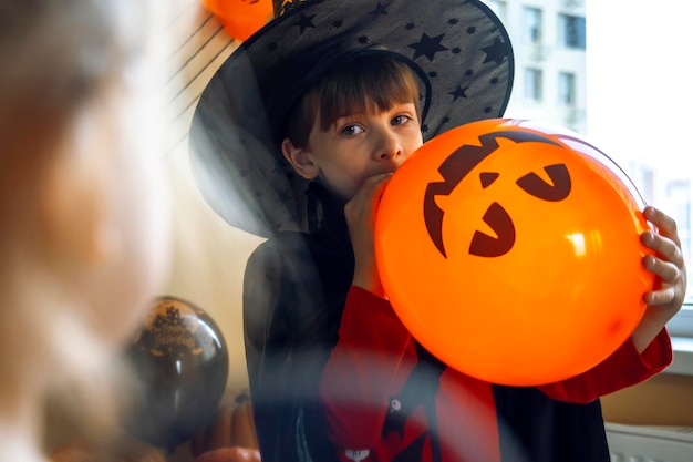 Le garçon souffle un ballon avec l'image d'une citrouille Jack l'enfant décore la maison pour Halloween