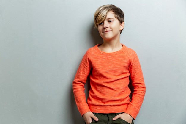 Un Garçon Souriant De 9 Ans Avec Une Coiffure à La Mode Dans Un Pull Orange Regarde Sur Le Côté