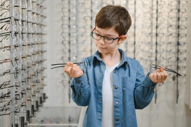 Garçon souriant choisissant des lunettes dans un magasin d'optique Portrait d'un enfant portant des lunettes dans un magasin d'optique