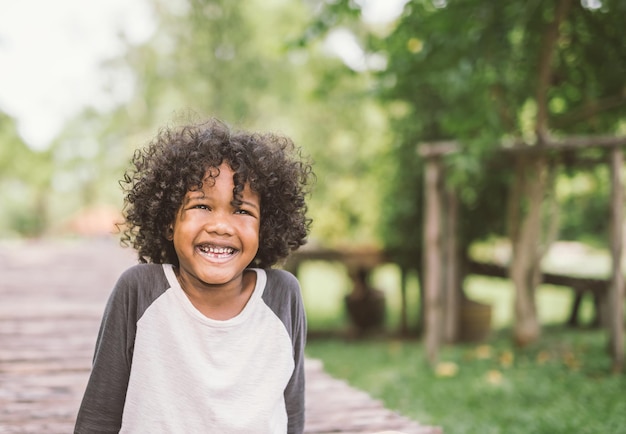 Un garçon souriant détournant son regard alors qu'il se tient dans le parc.