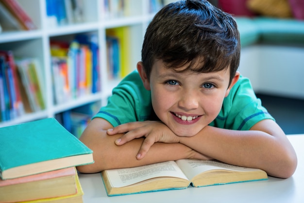 Garçon souriant avec livre dans la bibliothèque de l'école