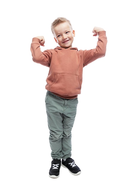 Un garçon souriant montre les muscles de ses bras Un beau mec dans un sweat à capuche marron et un pantalon gris Sport et santé Pleine hauteur Isolé sur fond blanc Vertical