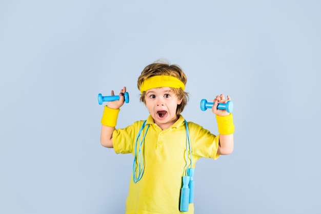 Garçon sportif d'enfant de forme physique avec la corde à sauter et le garçon d'entraînement de gymnastique d'haltères dans le sportwear avec le saut