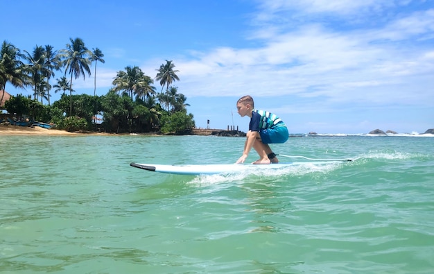 Le garçon surfe sur les vagues dans la mer bleue Plage de sable avec de beaux palmiersxA