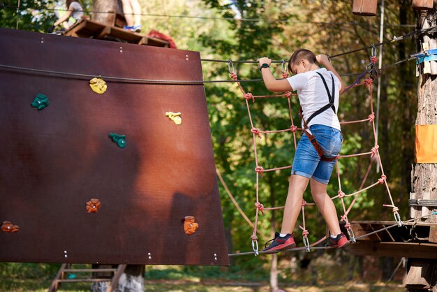 Le garçon surmonte l'obstacle dans le parc à cordes.