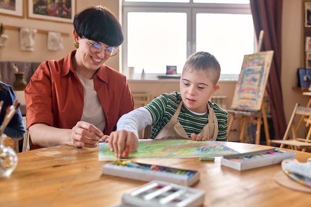 Un garçon avec le syndrome de Down apprécie le cours d'art avec son professeur.