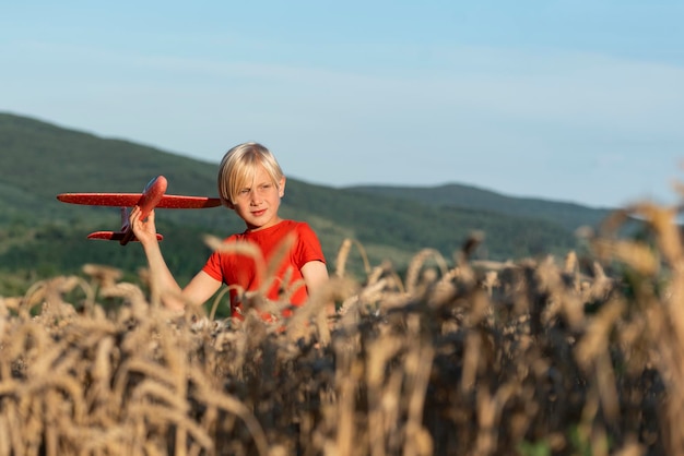 Garçon en T-shirt rouge joue avec un avion jouet dans un champ de blé Concept de vols et de voyages avec des enfants Fond de montagnes